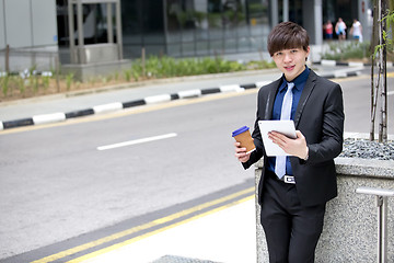 Image showing Young Asian business executive in suit holding tablet and coffee