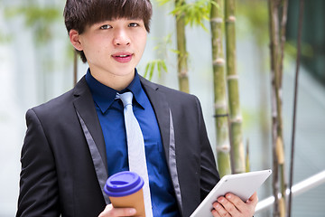 Image showing Young Asian business executive in suit holding tablet and coffee