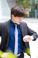 Image showing Young Asian business executive in suit looking at time