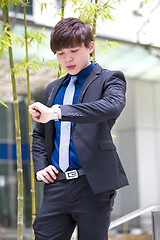 Image showing Young Asian business executive in suit looking at time