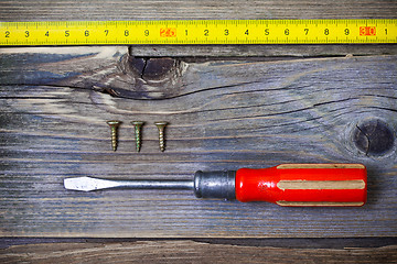 Image showing old screwdriver, three screws and measuring tape on textured boa