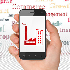 Image showing Finance concept: Hand Holding Smartphone with Industry Building on display