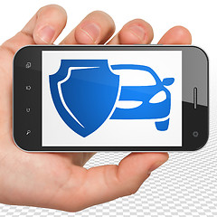 Image showing Insurance concept: Hand Holding Smartphone with Car And Shield on display