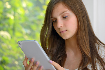 Image showing Serious young girl reading  on a tablet computer