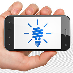 Image showing Business concept: Hand Holding Smartphone with Energy Saving Lamp on display