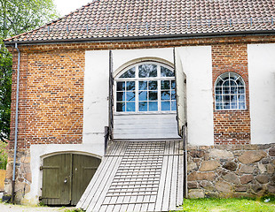 Image showing Old red brick building with wooden bridge path towards blue wind