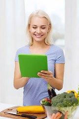 Image showing smiling young woman with tablet pc cooking at home