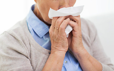 Image showing sick senior woman blowing nose to paper napkin