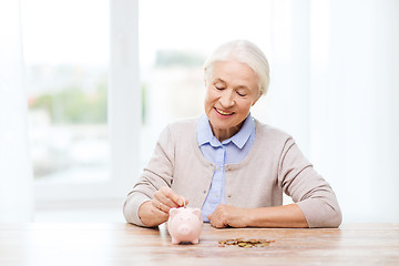 Image showing senior woman putting money to piggy bank at home