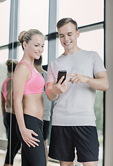 Image showing smiling young woman with personal trainer in gym