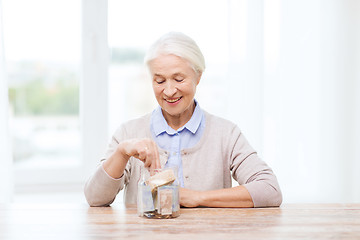 Image showing senior woman putting money into glass jar at home