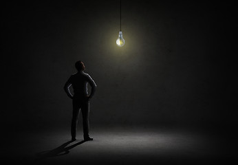 Image showing businessman looking at lighting bulb in dark room