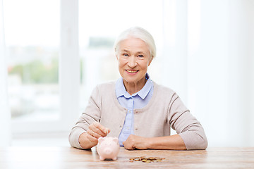 Image showing senior woman putting money to piggy bank at home