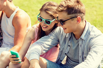 Image showing smiling friends with smartphone sitting in park