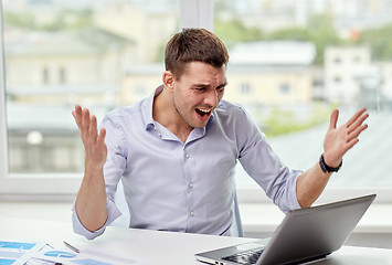 Image showing angry businessman with laptop and papers in office