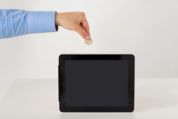 Image showing close up of hand putting coin into tablet pc