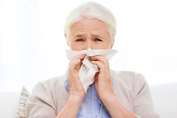 Image showing sick senior woman blowing nose to paper napkin