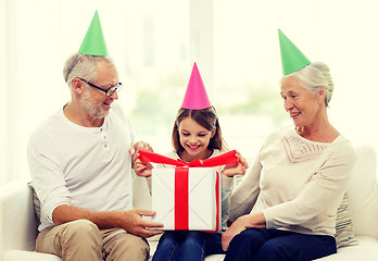 Image showing smiling family in party hats with gift box at home