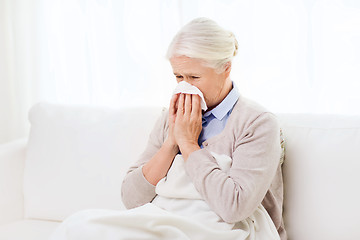 Image showing sick senior woman blowing nose to paper napkin