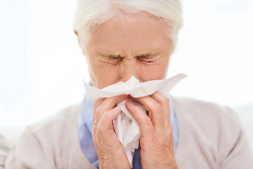 Image showing sick senior woman blowing nose to paper napkin