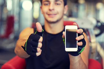 Image showing young man with smartphone showing thumbs up in gym