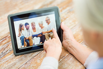 Image showing senior woman with family photo on tablet pc screen