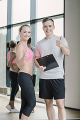 Image showing smiling young woman with personal trainer in gym