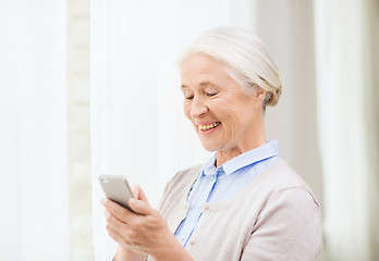 Image showing senior woman with smartphone texting at home