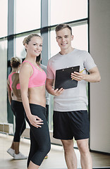 Image showing smiling young woman with personal trainer in gym