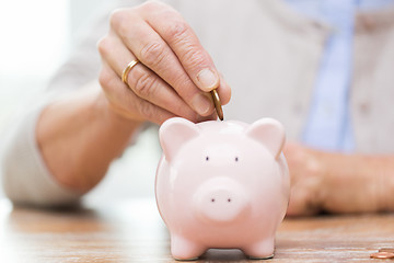 Image showing senior woman hand putting money to piggy bank