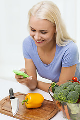 Image showing smiling woman with smartphone cooking vegetables