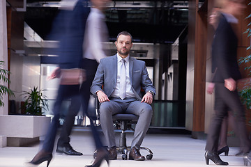 Image showing business man sitting in office chair, people group  passing by