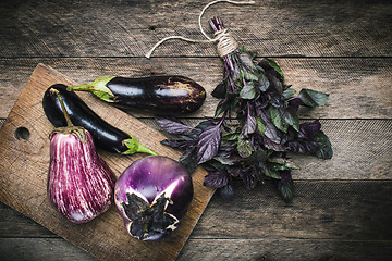 Image showing Aubergines and basil on chopping board and wooden table