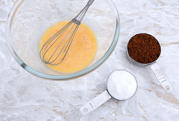 Image showing Beaten egg with whisk and measuring cups of sugar