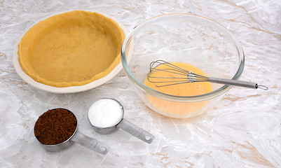 Image showing Lined pie dish, beaten egg and measuring cups of sugar