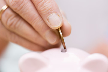 Image showing senior woman hand putting money to piggy bank