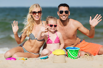 Image showing happy family with sand toys waving hands on beach