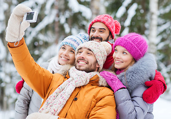 Image showing smiling friends with camera in winter forest