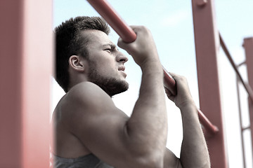 Image showing young man exercising on horizontal bar outdoors