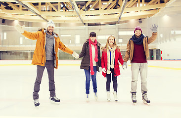 Image showing happy friends waving hands on skating rink