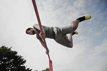 Image showing young man exercising on horizontal bar outdoors