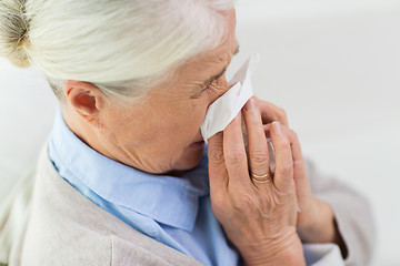 Image showing sick senior woman blowing nose to paper napkin