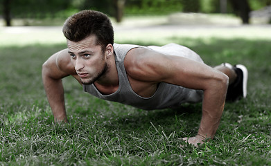 Image showing young man doing push ups on grass in summer park