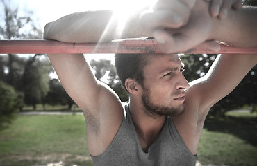 Image showing young man exercising on horizontal bar outdoors