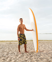 Image showing smiling young man with surfboard on beach