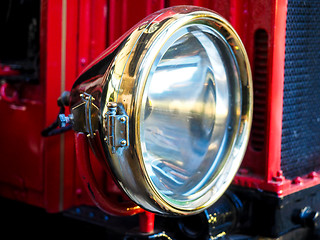 Image showing Closeup of brass headlight with glass on old red vehicle 
