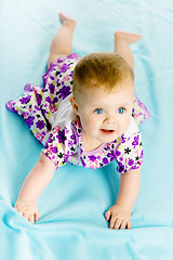 Image showing baby girl in a dress creeps on the blue coverlet