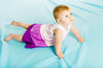 Image showing baby girl in a dress creeps on the blue coverlet