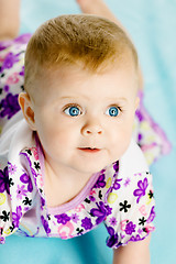 Image showing baby girl in a dress creeps on the blue coverlet