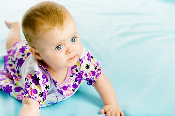 Image showing baby girl in a dress creeps on the blue coverlet